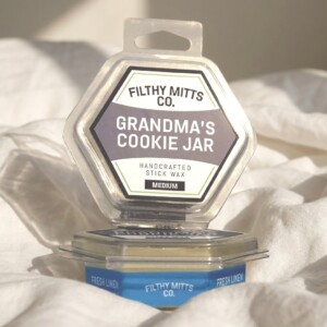 Actual photo of product with updated labeling/packaging processed through Kive.ai to generate realistic themed environment product images. Filthy Mitts Co. Grandma's Cookie Jar Stick Wax